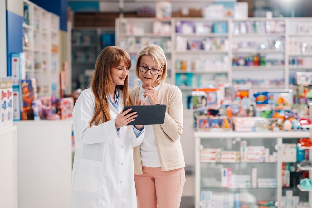 pharmacist,wearing,lab,coat,holding,digital,tablet,,helping,customer,with